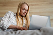 © Drobot Dean - Beautiful blonde happy woman using laptop while lying on bed