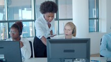 Serious Female Call Center Coach Helping Operator In Headset, Pointing At Monitor And Speaking. Front View. Female Business Leader Or Telemarketing Concept