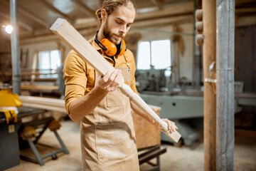 Wall Mural - Handsome carpenter in uniform working with wood, checking the quality of the wooden baluster at the joinery