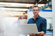 © Daniel Ingold/Westend61 - Smiling businessman holding laptop while standing in industry