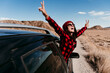 © Eva Blanco/Westend61 - Spain, Navarre, Female tourist leaning out of car window making peace sign gestures over dirt road in Bardenas Reales