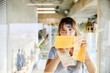 © Jo Kirchherr/Westend61 - Mature woman sticking sticky notes on glass material