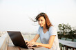 © Jo Kirchherr/Westend61 - Smiling mature woman using laptop while sitting on building terrace against clear sky