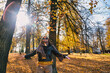 © Konstantin Trubavin/Westend61 - Happy woman standing with arms outstretched under falling dry autumn leaves while against trees at park