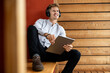 © peter scholl/Westend61 - Man wearing headphones with digital tablet looking away while sitting at home