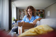 © Rainer Berg/Westend61 - Woman opening box while sitting on sofa at home