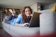 © Rainer Berg/Westend61 - Smiling woman using laptop while lying on sofa at home