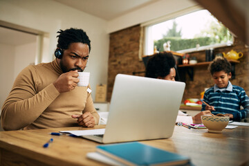 Wall Mural - African American father drinking tea while working on laptop at home.