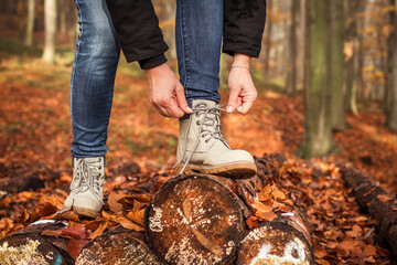 Wall Mural - woman tying shoelace on her hiking boot. tourist is getting ready for autumn hike in forest