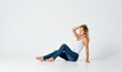 © SHOTPRIME STUDIO - a woman sits on the floor on a light background in jeans and a t-shirt side view
