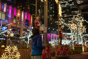 A boy wearing a face mask outside looking at Christmas lights