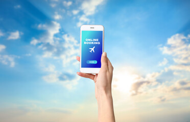 Wall Mural - Hand of woman with mobile phone against blue sky. Concept of online booking