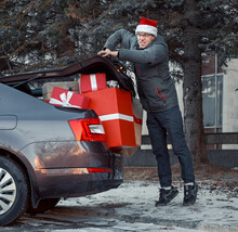 Man Trying To Close The Trunk Of A Car Filled With Boxes After Shopping. Too Many Purchases Are Too Much. A Full Trunk Of Holiday Packages And Boxes With Gifts. 