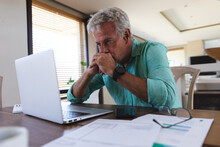 Worried Senior Caucasian Man Sitting At Table Using Laptop Paying Bills