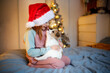 © natalialeb - Cute Funny Caucasian girl child in red Santa hat holding embrace puppy Jack Russell, funny New Year's photo of children and puppies, Christmas gift, dream about pet, puppy and child communications