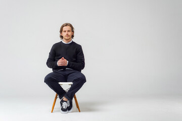 A business guy with a beard, on a white background in the studio, sits on a chair in jeans, a jacket