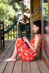 Wall Mural - Woman is knitting from pink yarn on the veranda of a wooden house.