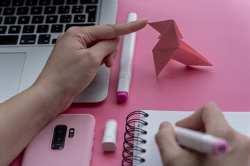 Wall Mural - Hand holding marker with a notebook, laptop, phone, and swan origami on pink background