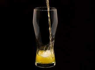 Pouring lager beer into a glass, isolated on black background, space for copy