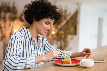 Beautiful happy curly woman smiling while drinking coffee with cake