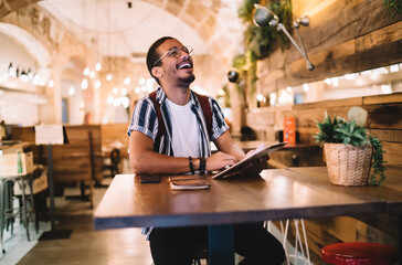 Happy ethnic man laughing and browsing tablet in cafe