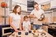 Happy young family, mother, father and daughter, cheerfully prepare cookies all together in light European kitchen