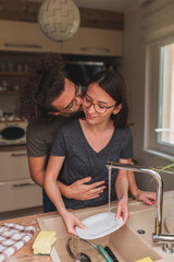 Man kissing woman while she is washing the dishes