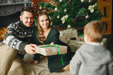 Wall Mural - Beautiful family sitting near Christmas tree. Cute mother in a green dress. Little boy with handsome father
