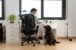 a young man is working from home with his computer in the office and his dog distracts him