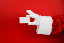 Santa Claus Hand Holding Blank Plastic Credit Card On Red Background With Clipping Path. Shopping, Sales, Giving Gift For Black Friday, Christmas And New Year Concepts