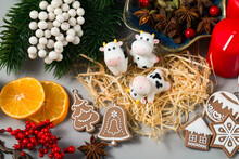 Three Cow Figures On A Christmas Background. Chinese New Year. Cute Smiling Toys, Gingerbread Decorations, Red Holly Berries, Tangerine Slices, Spices And Straw