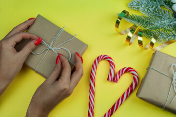 Christmas or new year festive background. Girl is packing a gift box with santa's lollipop cane sticks. White cane with red stripes on blue background with christmas tree and surprise