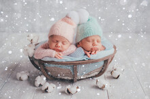 Twins Are Newborn Brother And Sister. Newborn Girl And Boy. Hats With White Fur Balls Sleep Sweetly In A Basket. Artificial Snow.