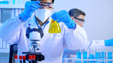 Asian scientist doing some research checking a liquid in a test flask at laboratory.