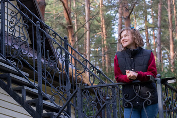 The girl stands on the black forged stairs of the cottage.