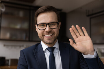 Wall Mural - headshot portrait of smiling young caucasian businessman wave at camera talk on video call. profile 