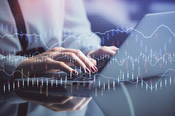 Double exposure of businesswoman hands typing on computer and financial graph hologram drawing. Stock market analysis concept.