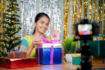 Girl opening gift in front of camera during christmas eve - concept of vlogging, girl got gift or present from subscribers during holyday season.