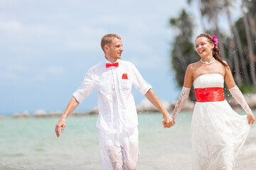 Happy groom and bride in wedding clothes on the sea beach in the tropics