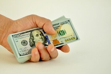 A stack of hundred-dollar bills in a man's hand close-up on a white background