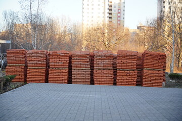 Pile of pallets with red bricks on city street. Building materials on construction site outdoor. Concept of constructing buildings.