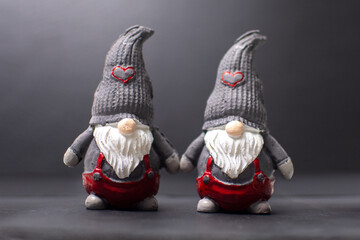 Two scandinavian traditional father christmas Tomte holding their hands standing still wearing gray conical hat with red heart isolated dark gray background