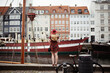 woman with long blonde hair and sun hat in copenhagen in front of colorful buildings traveling on vacation 