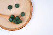 Spirulina tablets in wooden spoon on round stand, white background. Nutrition, vitamin, immunity concept. Top view, flat lay, copy space