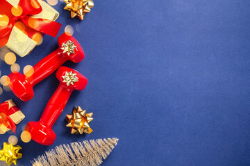 Wall Mural - Exercise, fitness and development of the concept of a happy Christmas and a happy New year. Red dumbbells, bows, Christmas tree and gifts with red ribbons on a dark blue background, bokeh. Flat lay