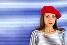 Portrait Of Woman That Looks Like She Is Caught In A Lie. She Is Wearing Red Beret And Striped Shirt. Facial Expression And Body Language.