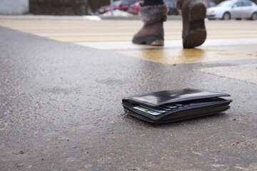 the lost wallet lies on the road near the crosswalk, and in the background are the legs of a leaving