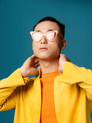 guy holding his hands behind his head yellow jacket asian blue background