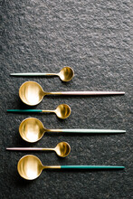 Stylish Colorful Spoons Of Various Sizes On A Black Background. Flat And Top View. Dark And Morbid Vibes