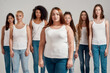 © Svitlana - Portrait of beautiful young caucasian plus size woman in white shirt looking at camera. Group of diverse women posing, standing isolated over grey background